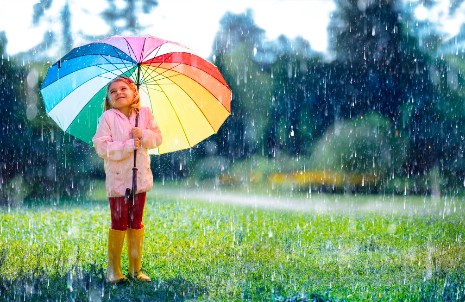 Ein junges Mädchen steht mit einem bunten Regenschirm im Regen